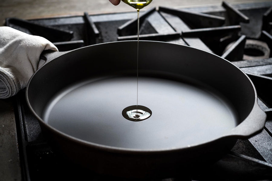 Stream of oil falling into the machined-smooth surface of a Field Skillet on a gas range