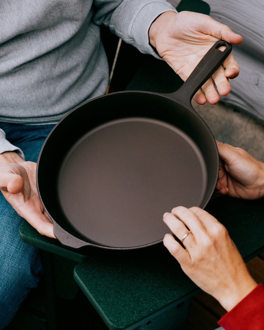 Overhead of two people passing a Field Skillet between their hands over a green chair