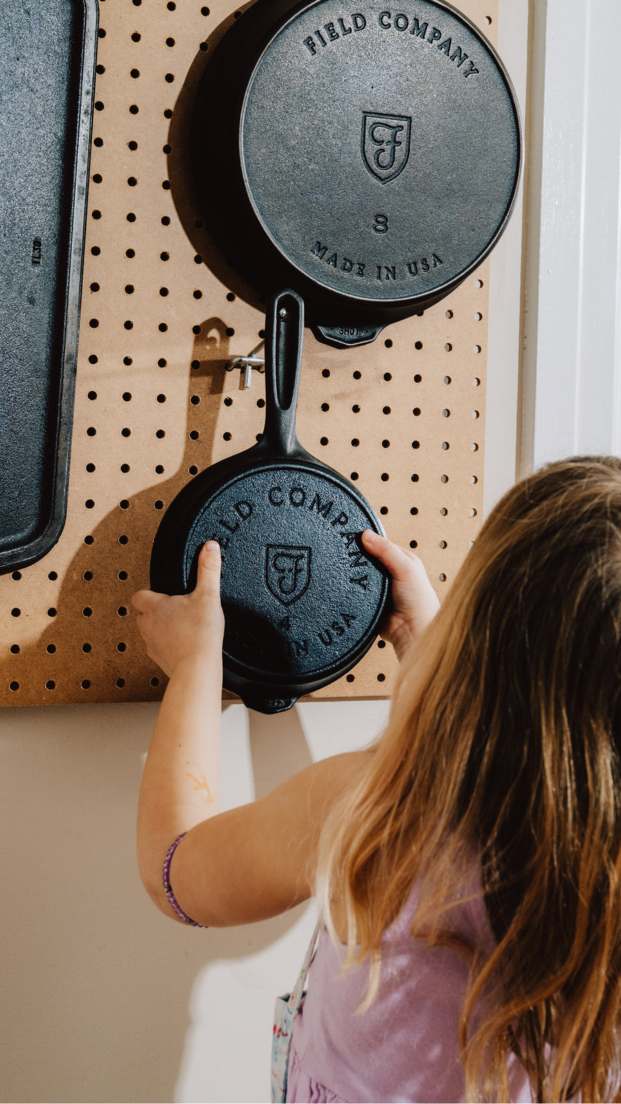 Child hanging a small Field Company skillet on a pegboard below the No.8, stamped undersides facing out