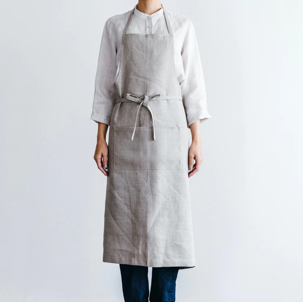 Model wearing the Field Company gray linen full length apron tied at the waist over a white shirt