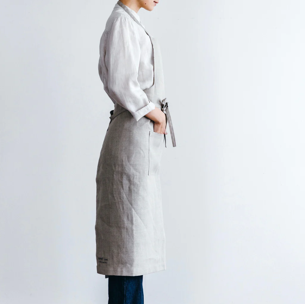 Side view of the Field Company linen full length apron in natural gray, tied at the waist over a white shirt
