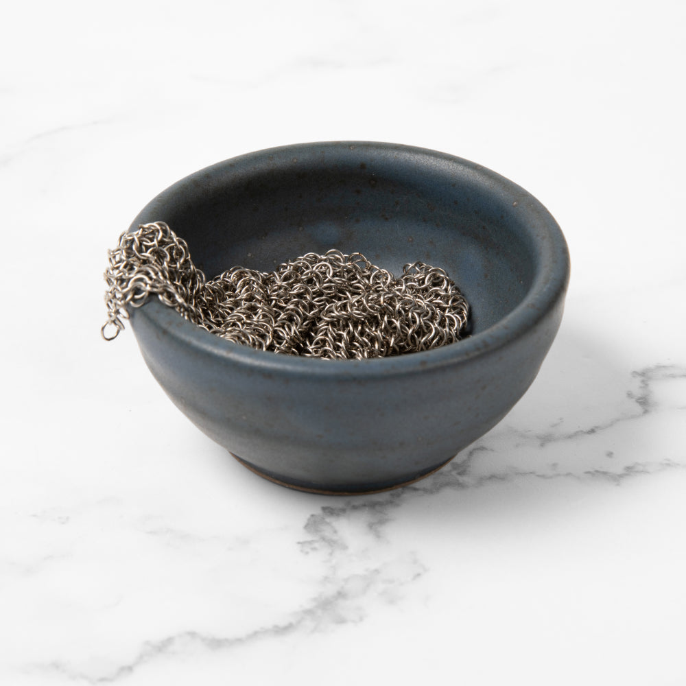 Tiny Field ceramic bowl in slate blue holding a chain mail scrubber, on a marble counter