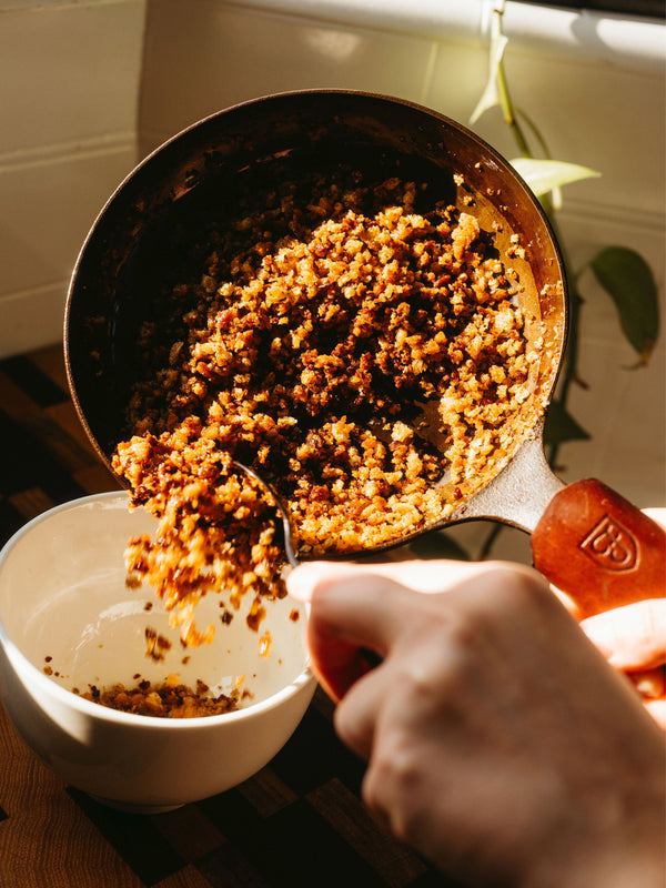 Person spooning toasted breadcrumbs from a Field Skillet with a leather handle cover into a small bowl
