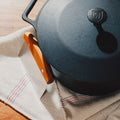 Overhead detail of the No.10 Field Dutch Oven lid with the wood-handled bench scraper on a striped linen towel thumbnail