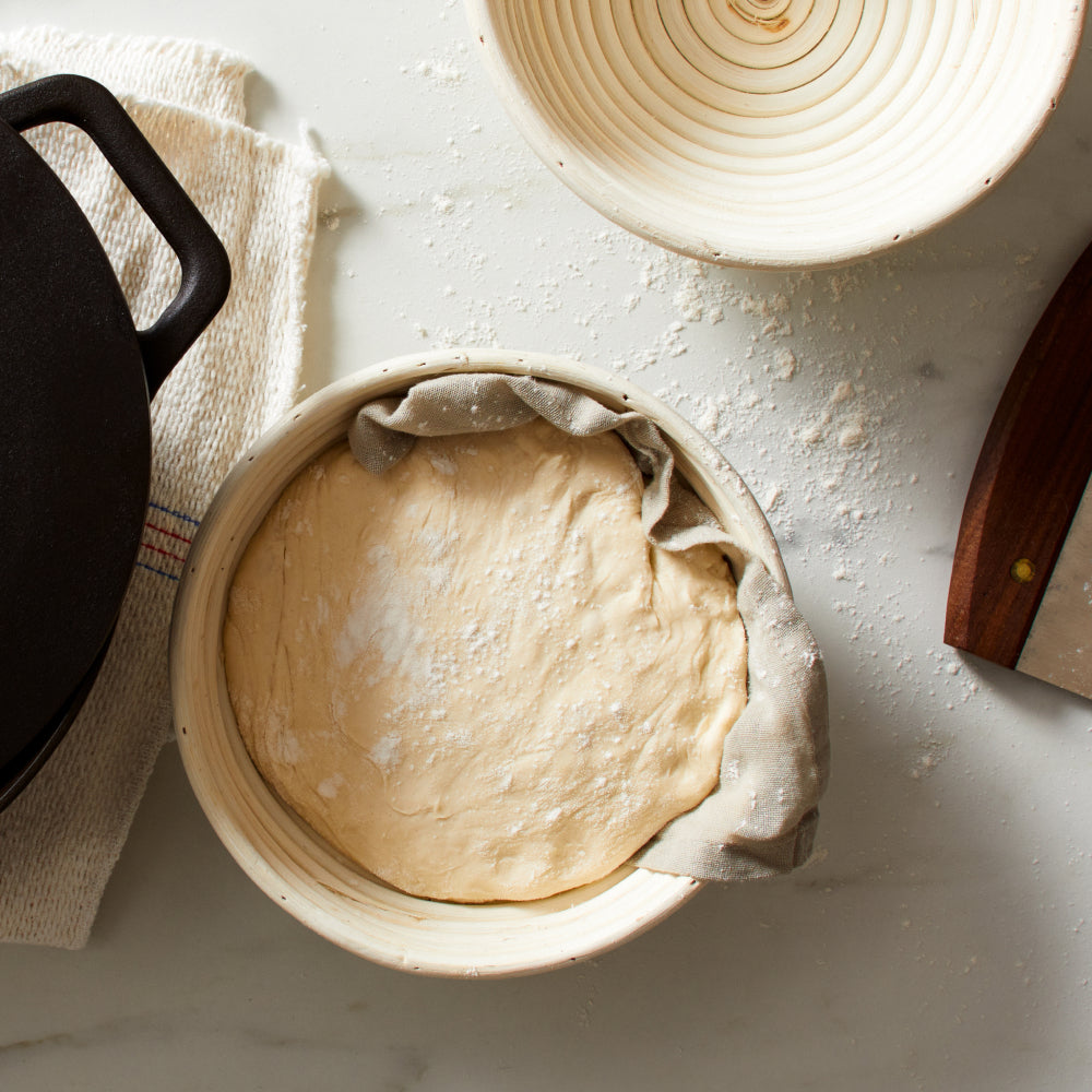 Bread dough proofing in cloth-lined baskets beside the Field Dutch Oven on a flour-dusted counter