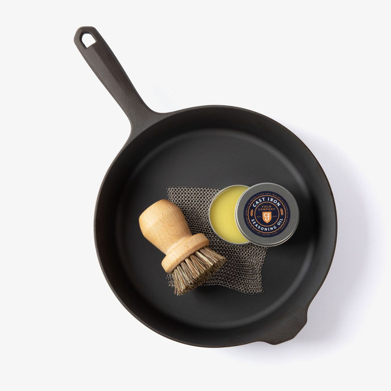 Overhead view of the No.8 Field Cast Iron Skillet holding the care kit scrub brush, chain mail, and seasoning oil