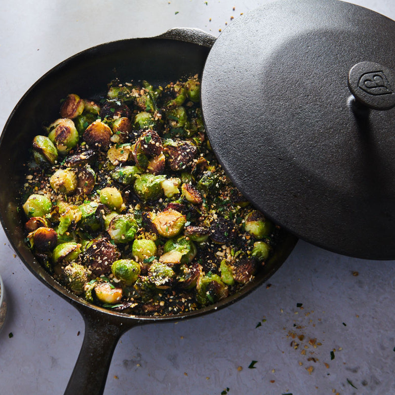 Crispy roasted brussels sprouts in the Field Skillet, its cast iron lid resting ajar