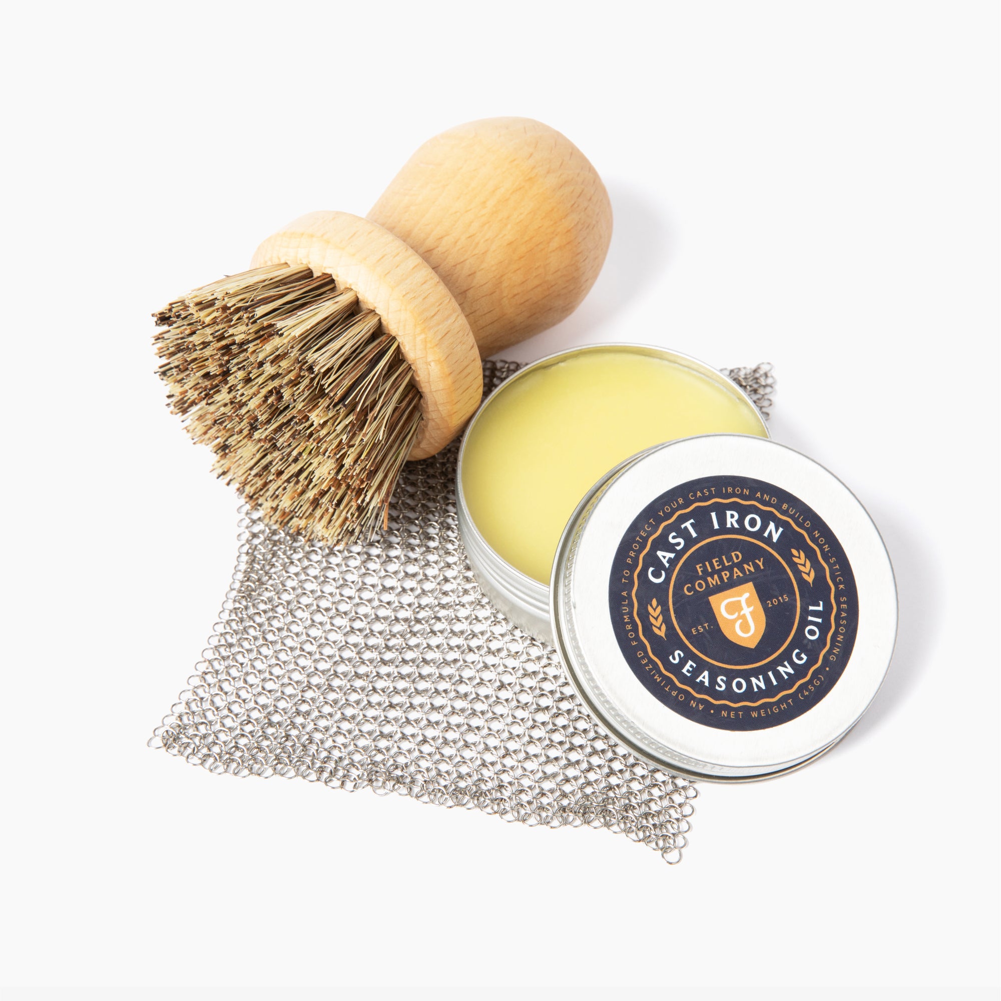 Open tin of Field Company Cast Iron Seasoning Oil with wood scrub brush and chain mail scrubber