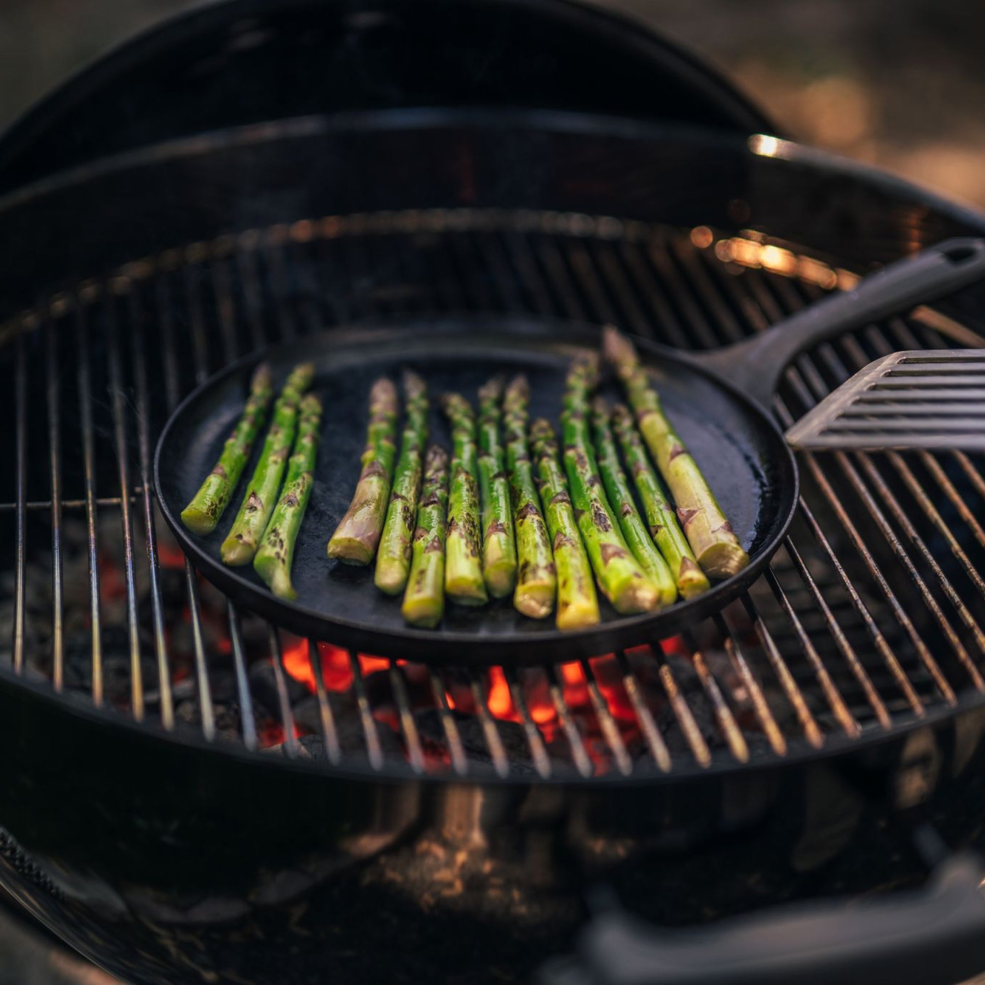 Asparagus spears grilling on the No.9 Field Round Cast Iron Griddle over glowing charcoal in a kettle grill
