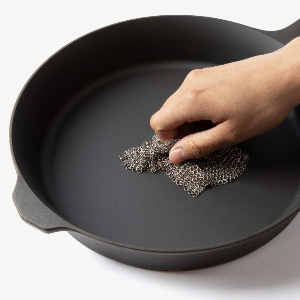 Hand scrubbing the cooking surface of a Field Skillet with the stainless chain mail scrubber