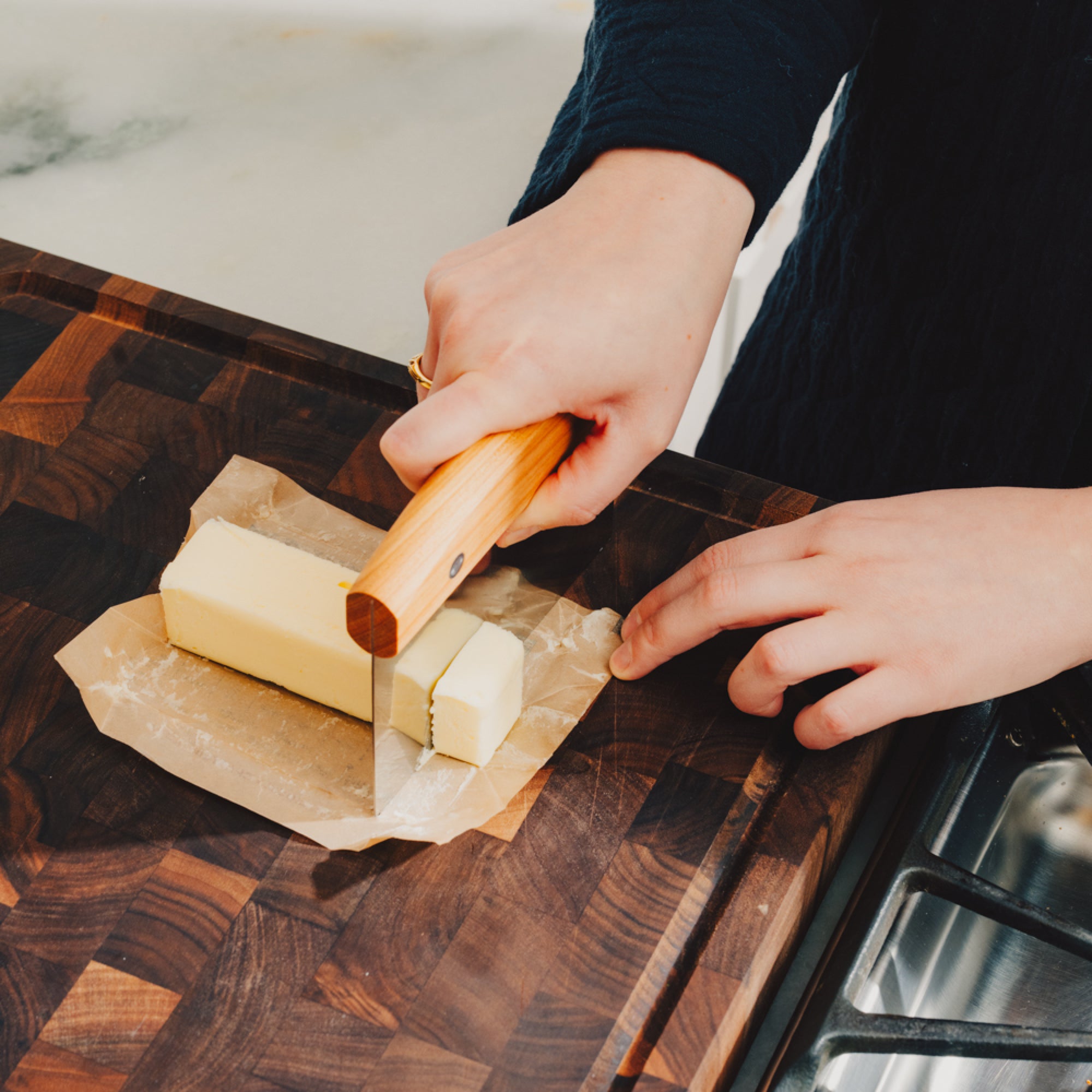 Hands portioning a stick of butter with the Field Bench Scraper on a walnut cutting board