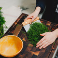 Hands scooping chopped dill with the Field Bench Scraper on an end-grain cutting board thumbnail