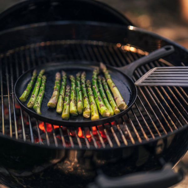 Grilling asparagus on a Field Company cast iron griddle over hot charcoal in a round grill