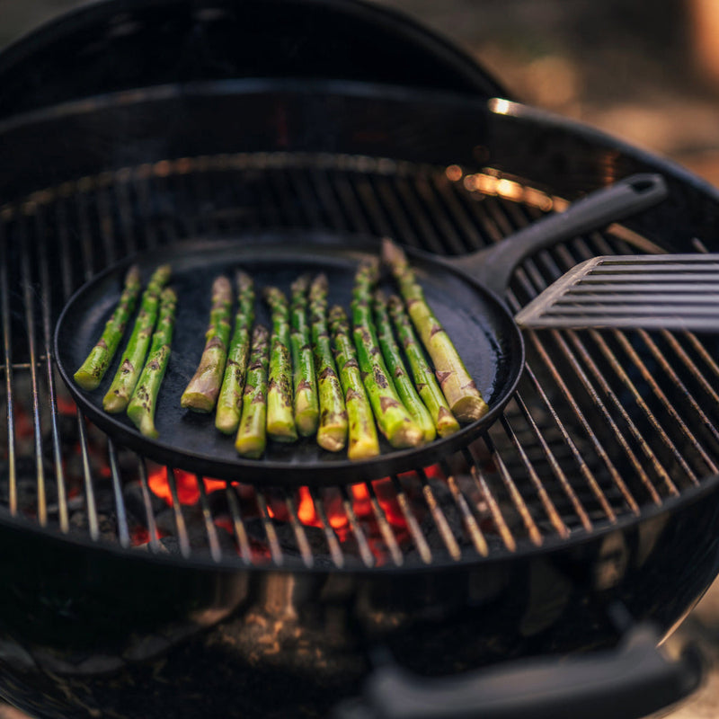 Grilling asparagus on a Field Company cast iron griddle over hot charcoal in a round grill