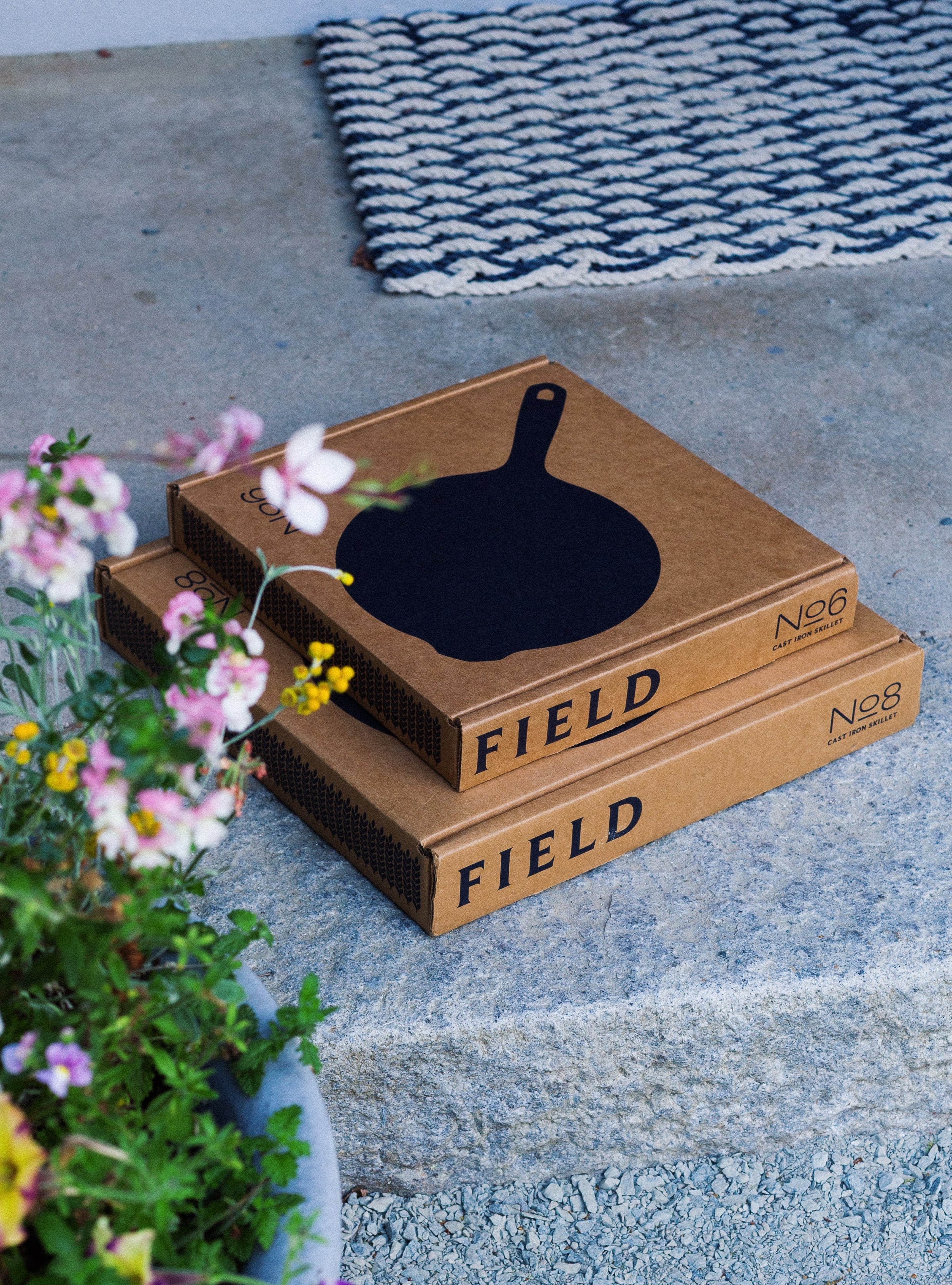 Two FIELD skillet boxes labeled No.6 and No.8 stacked on a stone step beside flowers and a doormat