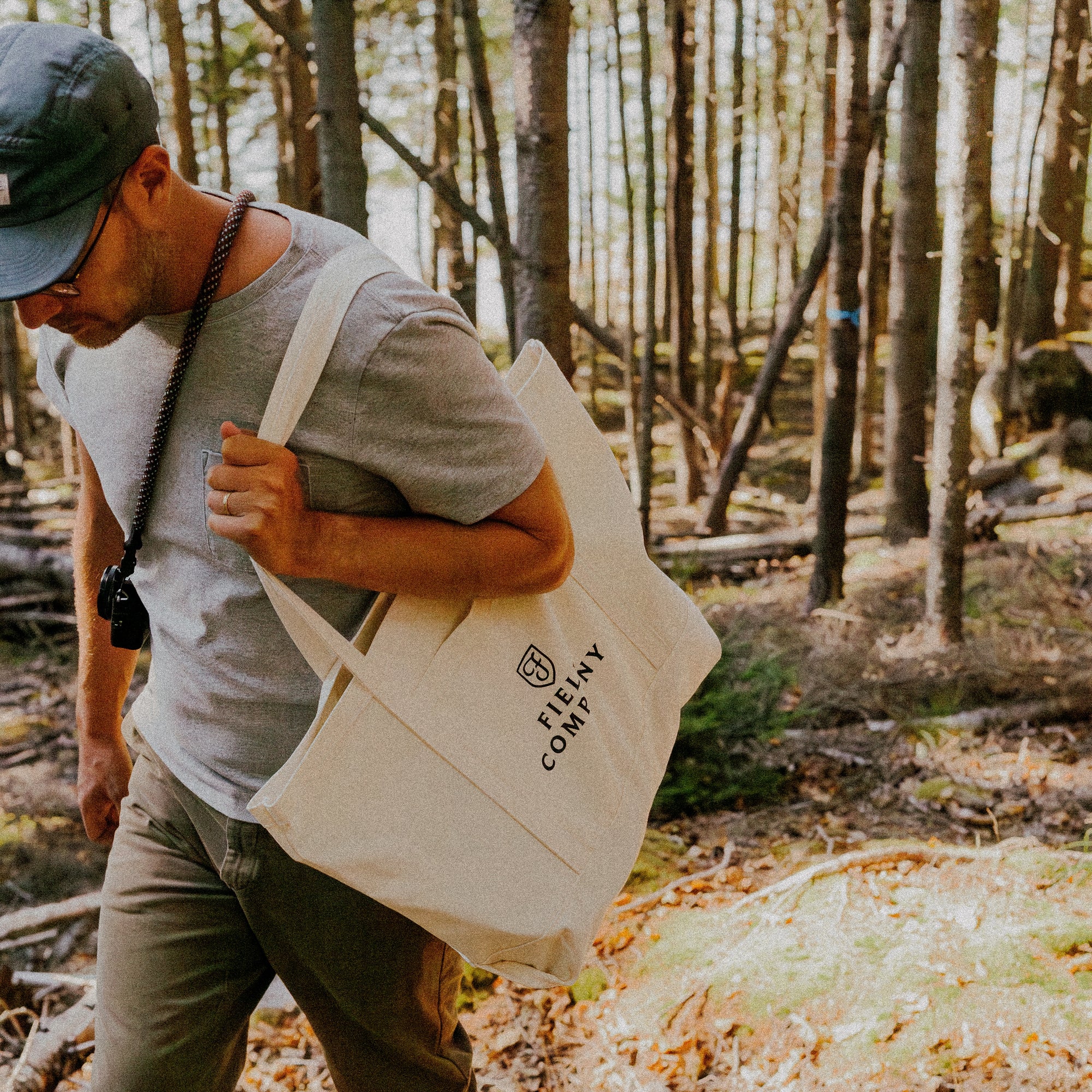 Man carrying the Field Market Tote over his shoulder while walking through the woods