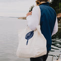 Person carrying the Field Market Tote with navy skillet graphic over one shoulder by the water thumbnail