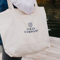Field Market Tote in natural canvas with navy logo, carried over the shoulder on a waterside dock thumbnail