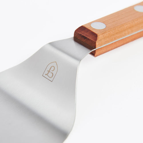 Close-up of the Field stainless steel spatula with engraved shield logo and riveted cherry wood handle