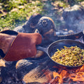 Person in a Field leather oven mitt holds a skillet of pistachios over a smoky open campfire thumbnail