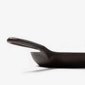 Close-up profile of the Field Skillet handle and hanging hole, curved wall rising behind thumbnail