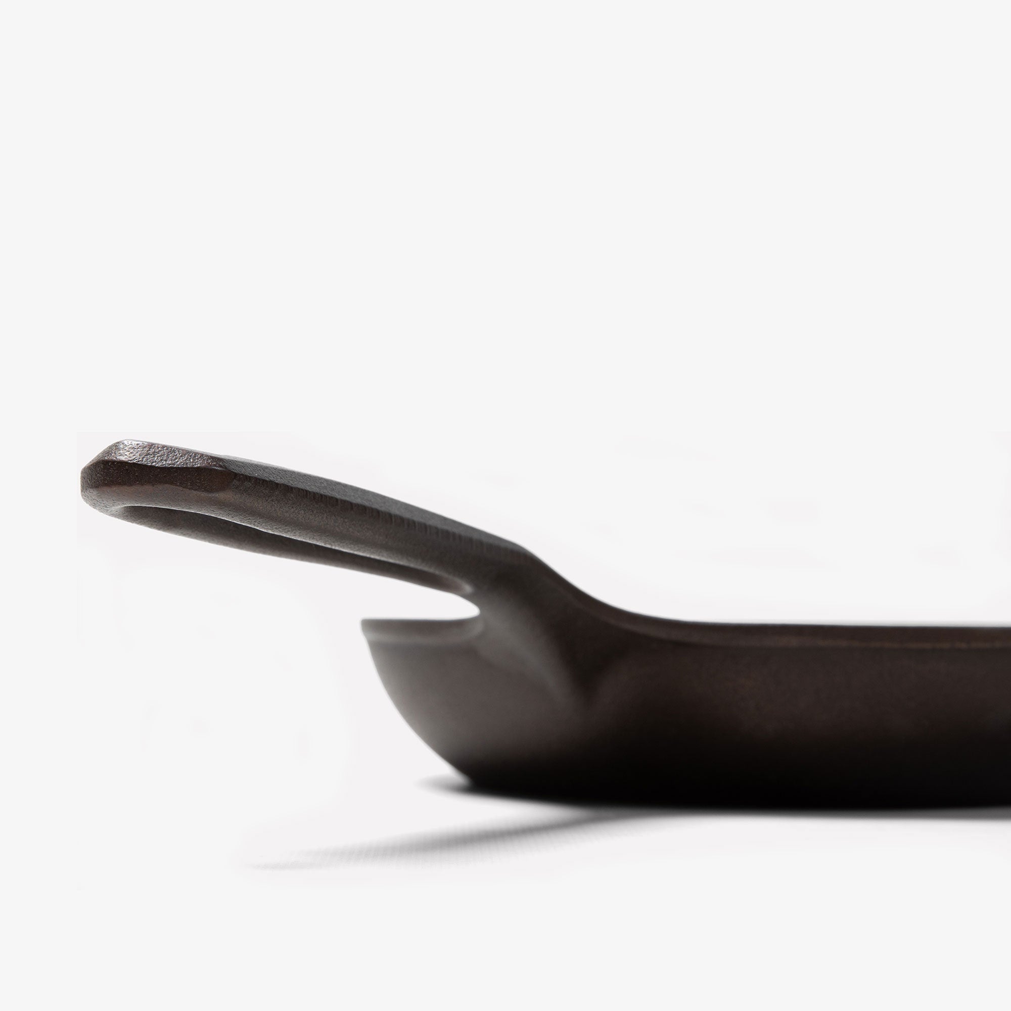 Close-up profile of the Field Skillet handle and hanging hole, curved wall rising behind