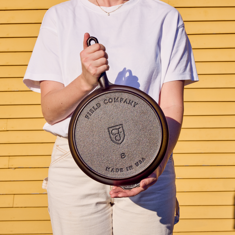 Person holding a No.8 Field Cast Iron Skillet upside down to show the stamped underside, outdoors in sunlight