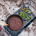 Chili simmering in the No.10 Field Dutch Oven on a campfire grate beside a plate of charred peppers thumbnail