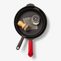 Nested Field Skillets with scrub brush, chain mail, seasoning oil tin, and a red leather handle cover, overhead view thumbnail