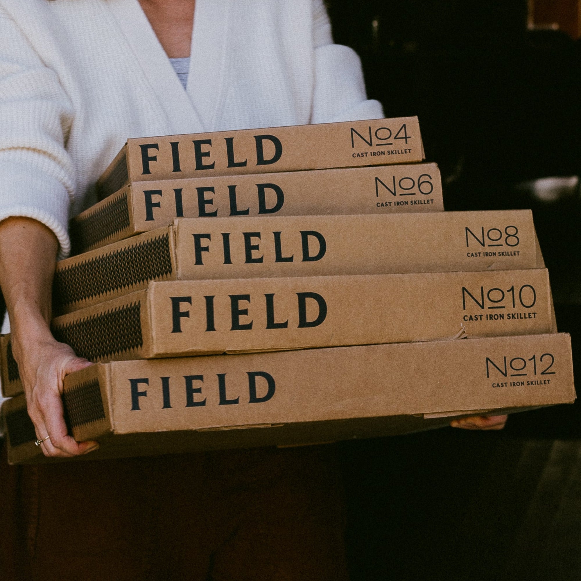 Person carrying a stack of five Field Cast Iron Skillet boxes from No.4 up to No.12