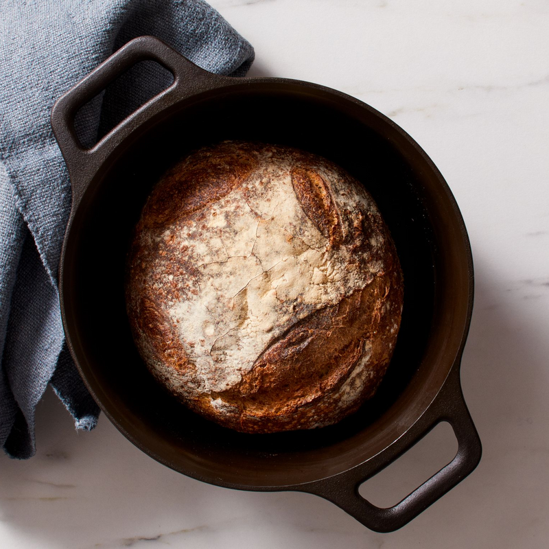 Crusty round loaf baked in the No.8 Field Cast Iron Dutch Oven, blue linen towel alongside