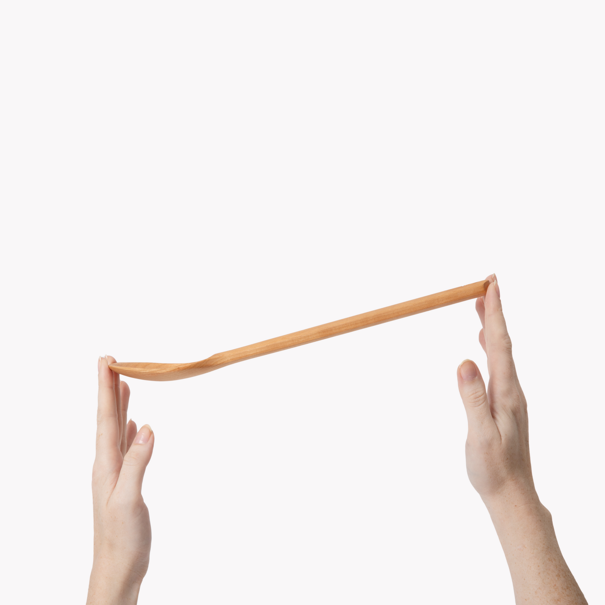 Two hands balancing a Field cherry wood spoon horizontally between fingertips
