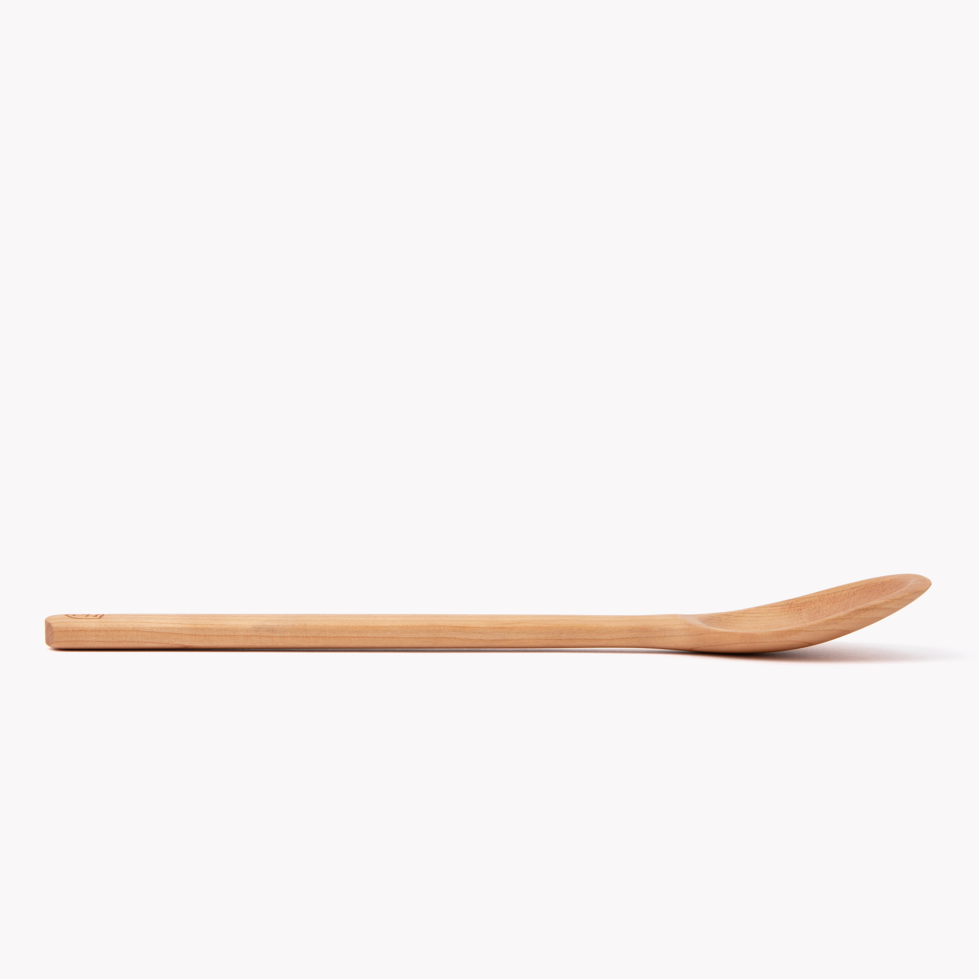 Side profile of a cherry wood Field spoon lying flat, showing its slim handle and shallow bowl