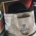 Field Market Tote holding a boxed No.8 Cast Iron Skillet with care kit, resting against a striped blanket thumbnail