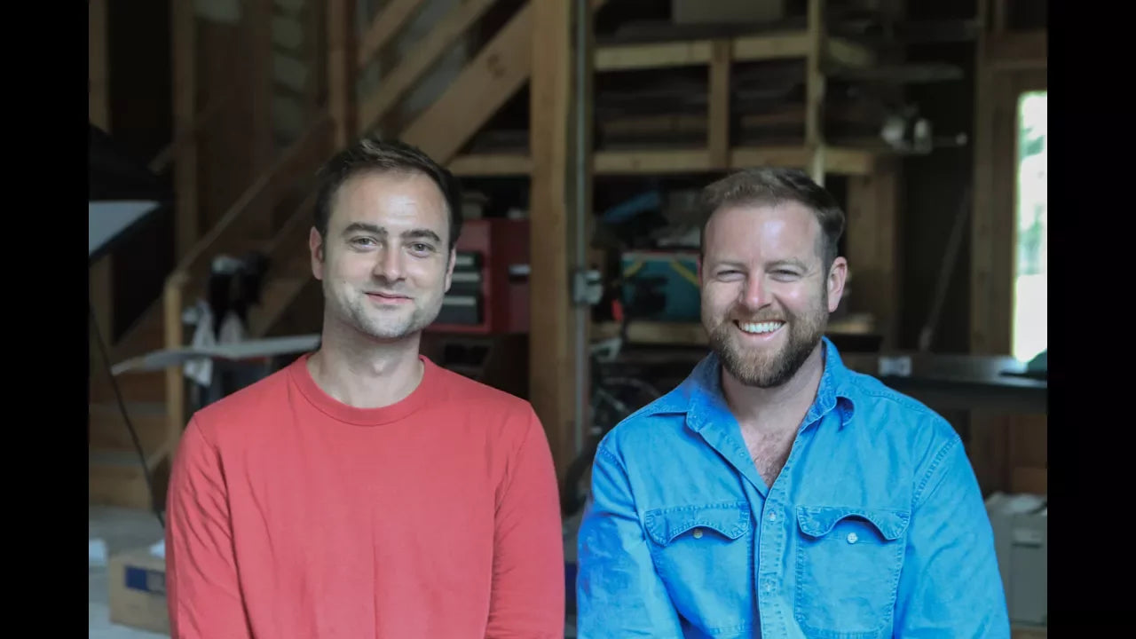 Field Company founders smiling side by side in a workshop, one in a red sweater and one in a blue shirt