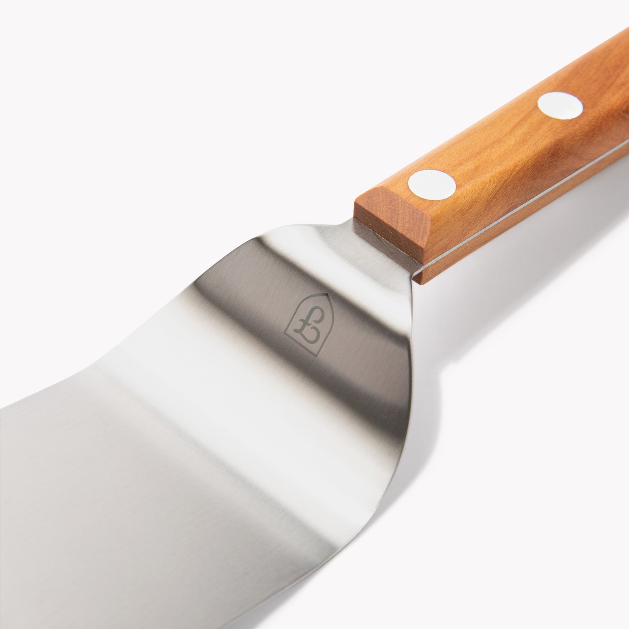 Close-up angled view of the Field Mini Turner's stainless blade, stamped shield logo, and cherry wood handle
