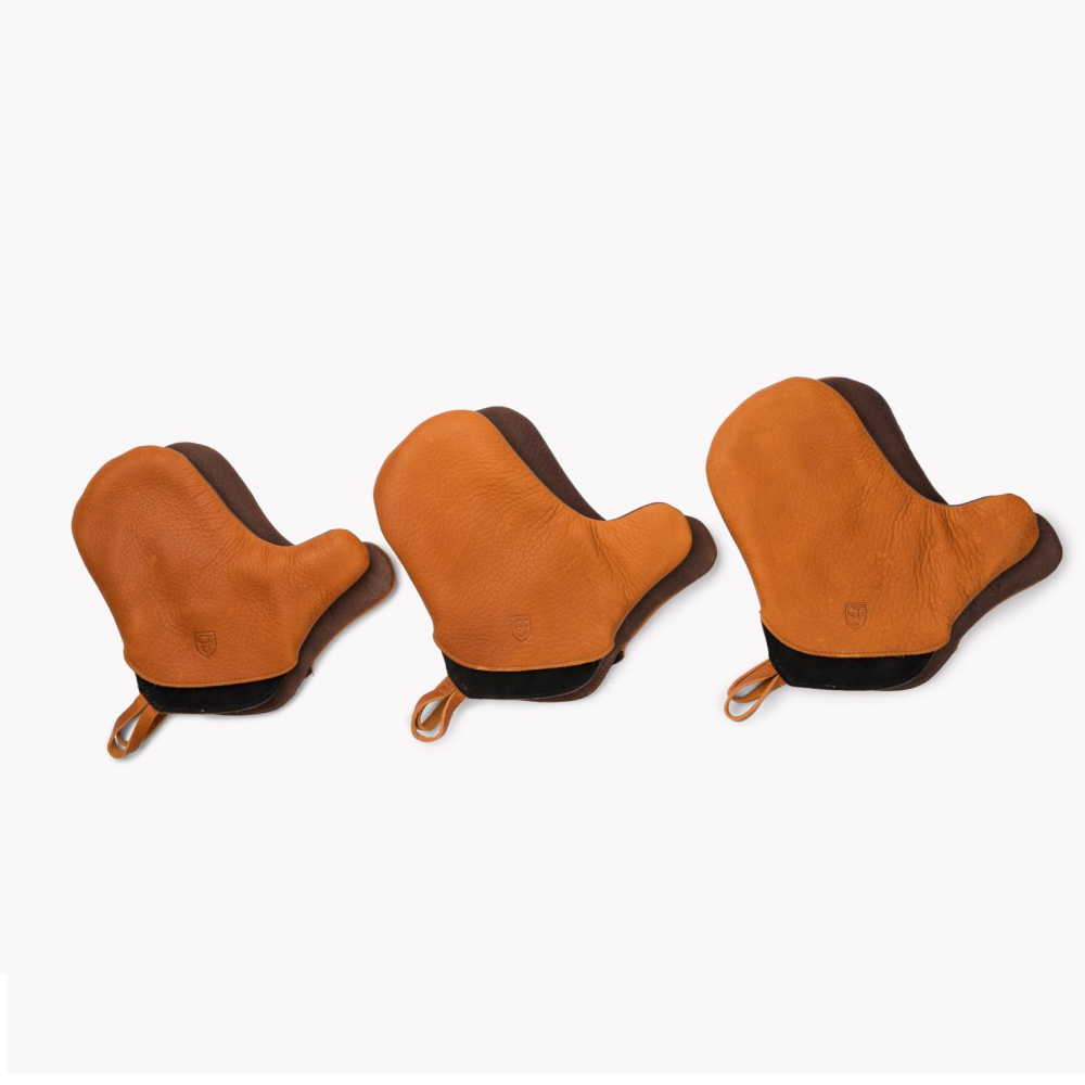 Three tan leather Field oven mitts in a row with dark cuffs and hanging loops, on white background