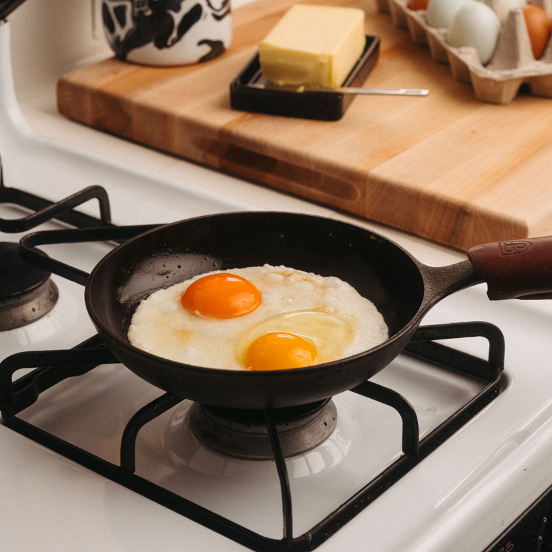 Two fried eggs cooking in the No.5 Field Cast Iron Chef Skillet on a white gas stovetop