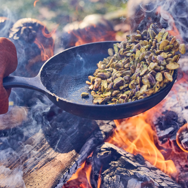 Person toasting nuts in a Field Skillet over open campfire flames