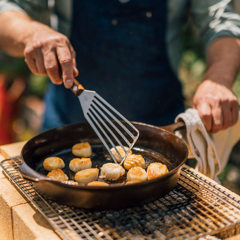 Person flips seared scallops with a Field slotted turner over the DIY Konro grill outdoors