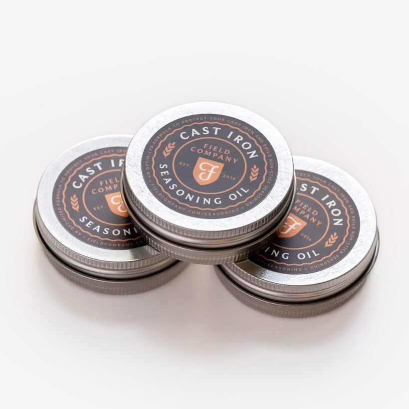 Three stacked tins of Field Company Cast Iron Seasoning Oil on a white background