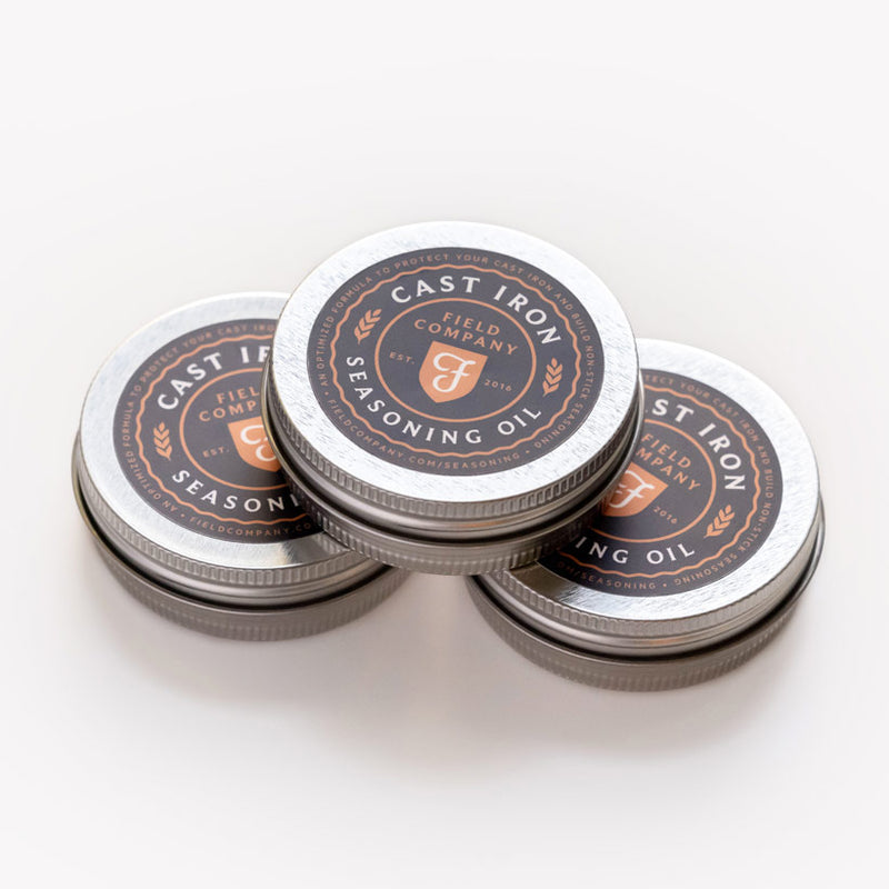 Three stacked tins of Field Company Cast Iron Seasoning Oil on a white background