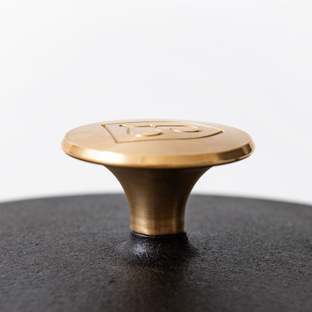 Close-up of the bronze Field lid knob mounted on a cast iron lid, engraved logo on its flared top