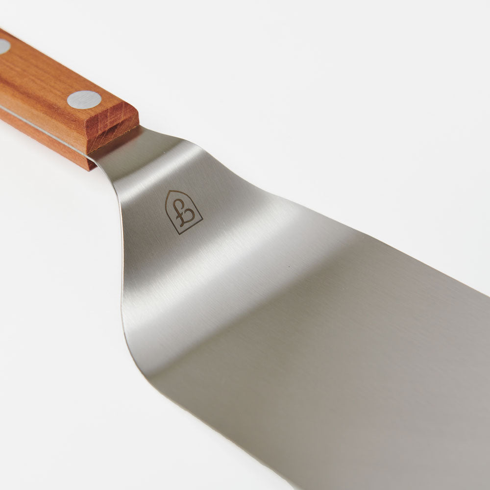 Close-up of the Field Griddle Turner's offset stainless blade and riveted cherry wood handle