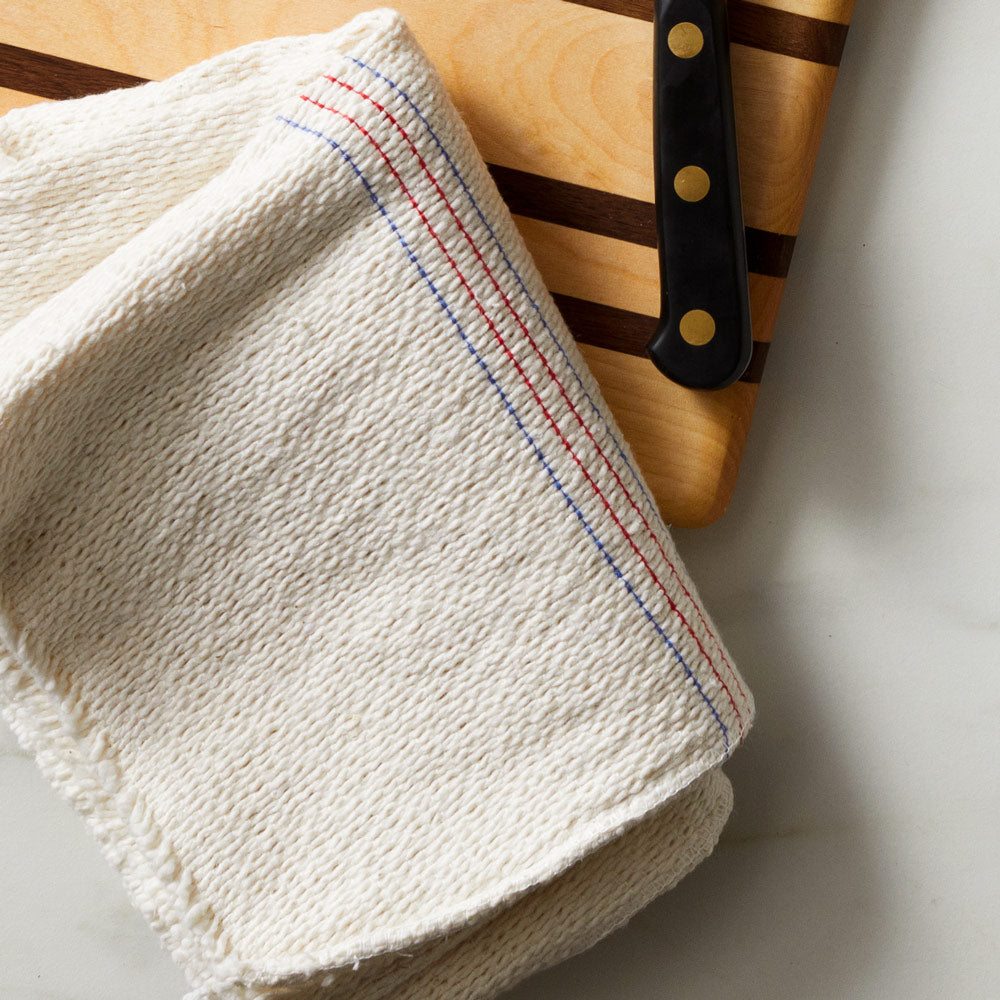 Field Company XL Cleaning Cloth with red and blue stripes folded on a cutting board beside a knife